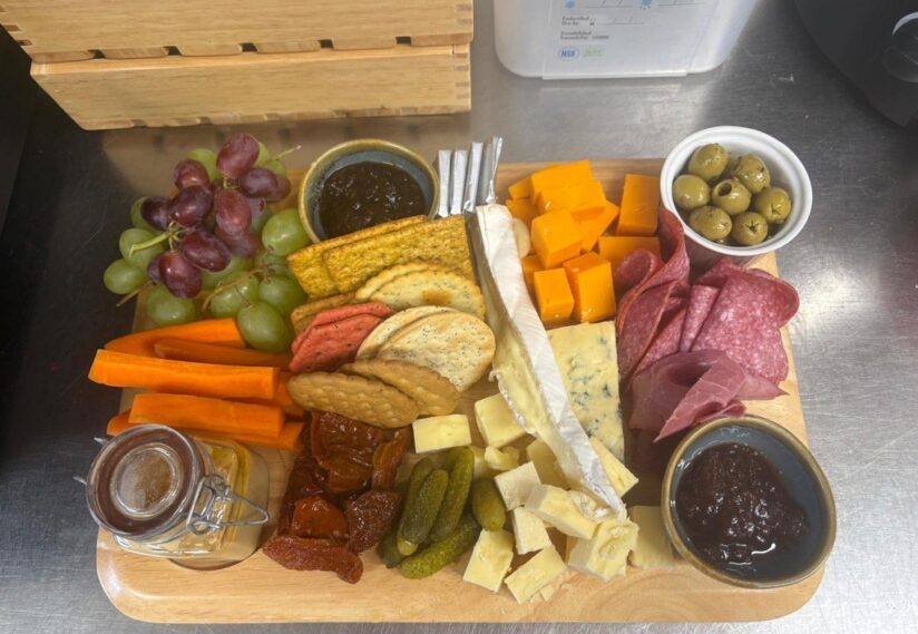 tray filled with cheese and biscuits and fruits, carrot sticks, grapes, ham, chuntney