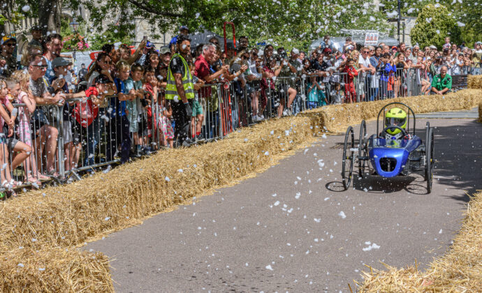 soapbox derby kart in blue and driver with people on the sidelines