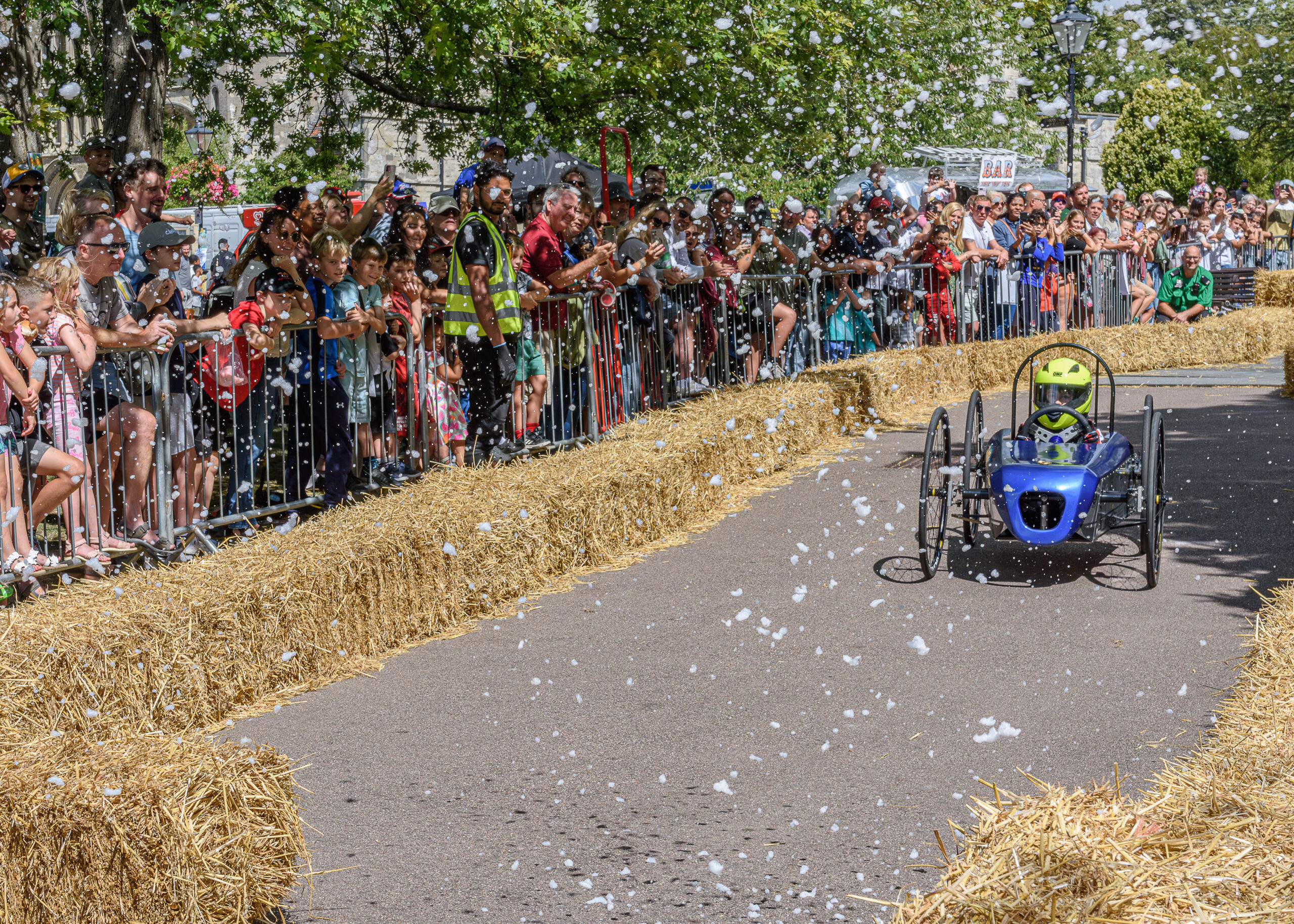 soapbox derby kart in blue and driver with people on the sidelines