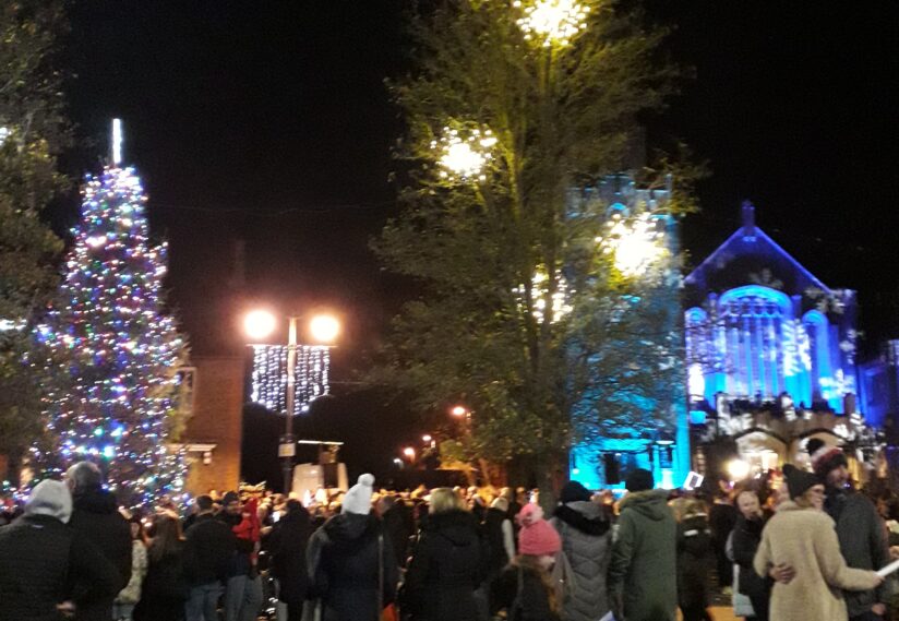 Christmas tree in The Square with lights on the church and people