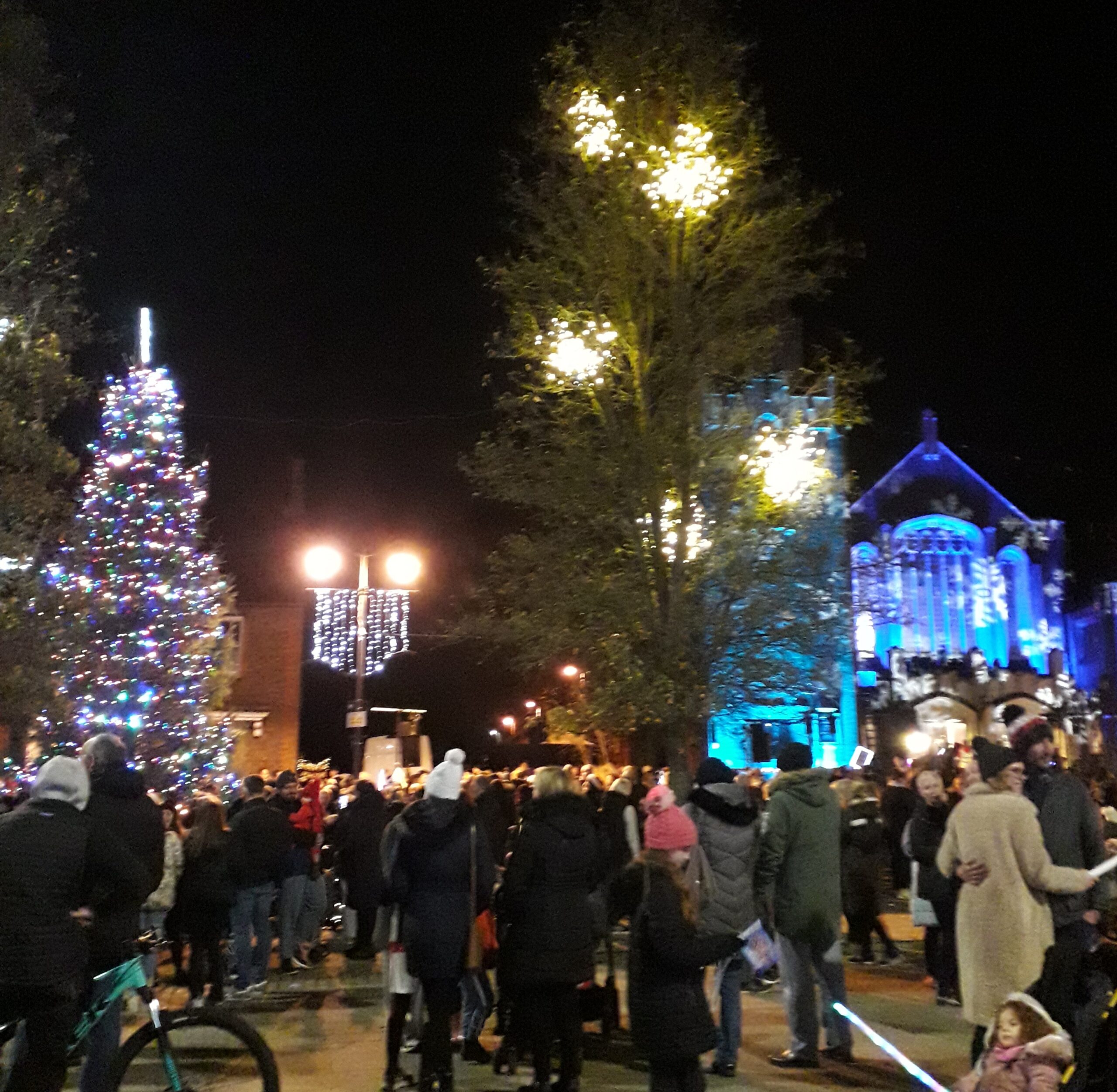 Christmas tree in The Square with lights on the church and people