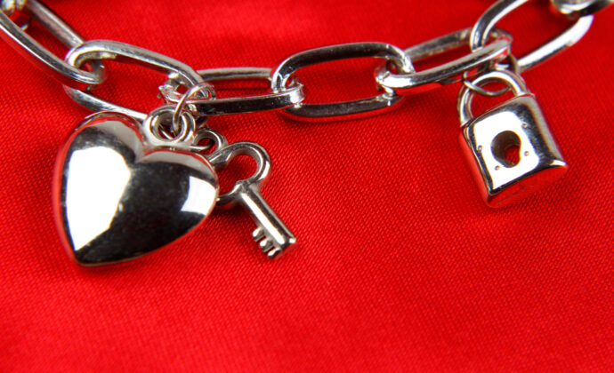 Silver charm bracelet on vibrant red background, featuring a heart, key, and padlock. Reflective, romantic, and elegant theme.