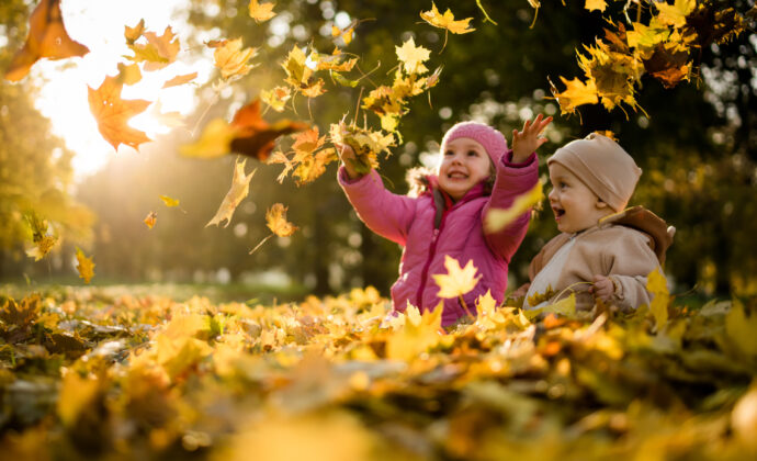 Siblings playing with maple leaves in autumn park