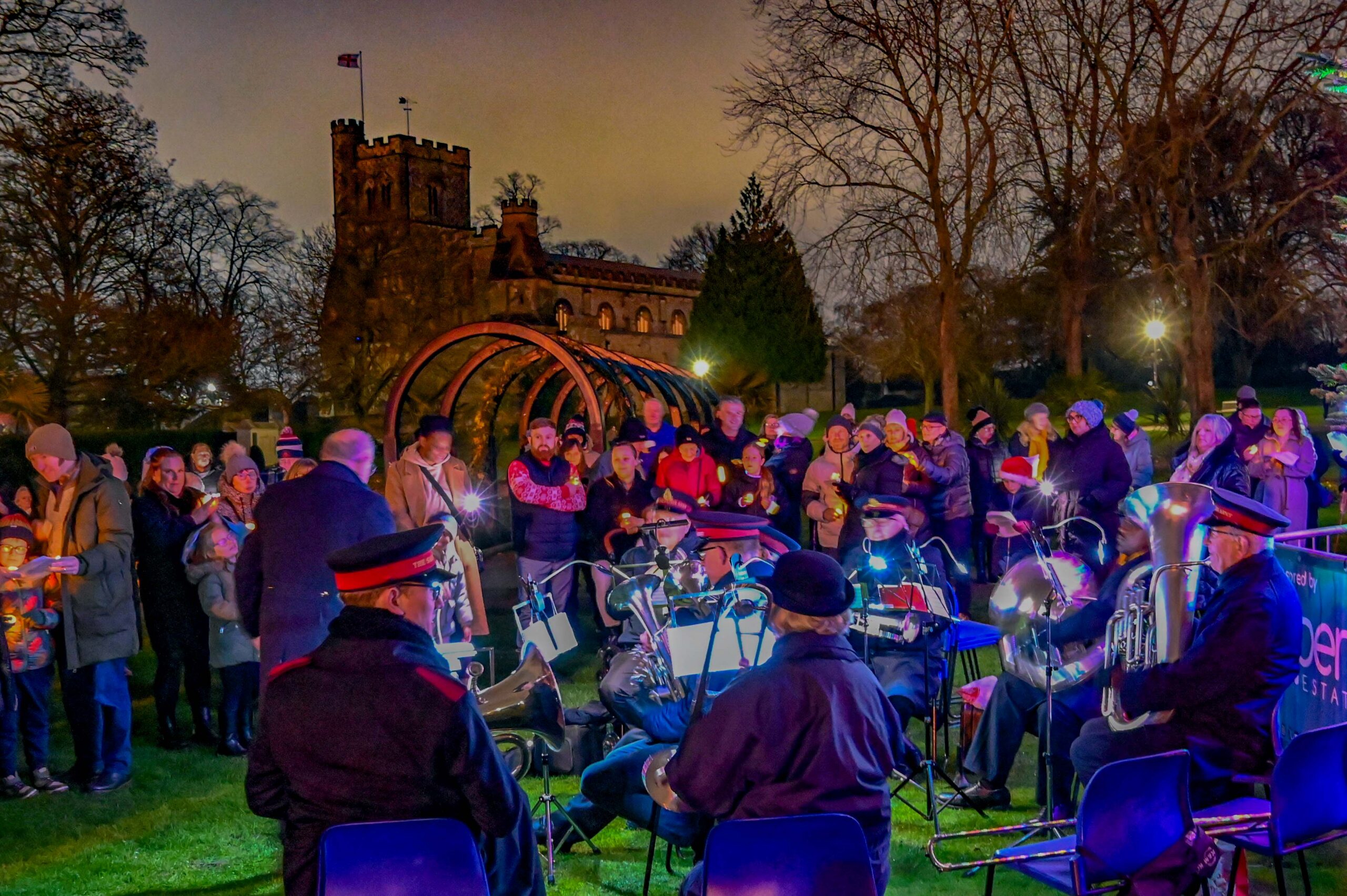 A brass band performs for a crowd gathered outdoors at night in front of an illuminated church.