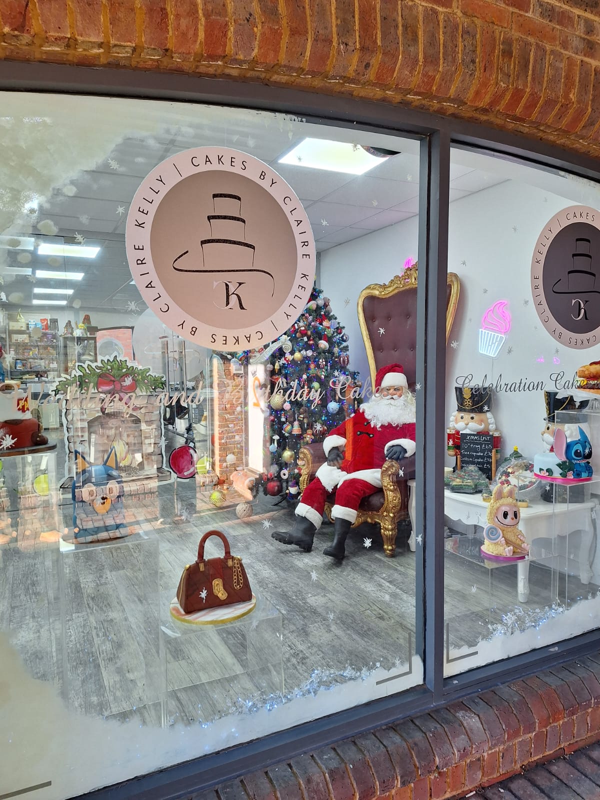 Christmas Window with Santa in a chair next to a large Christmas tree, Santa is eating cake and having a cup of tea