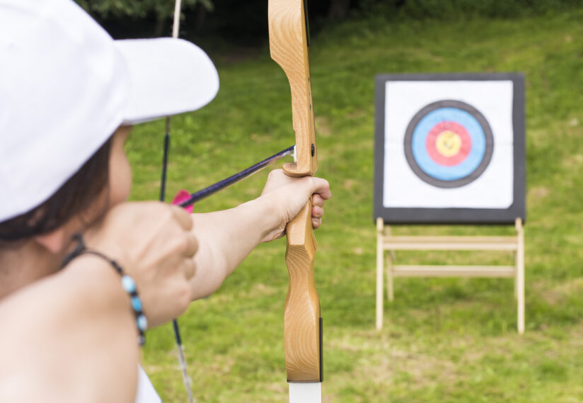 A young female archer holding a bow aiming at a target
