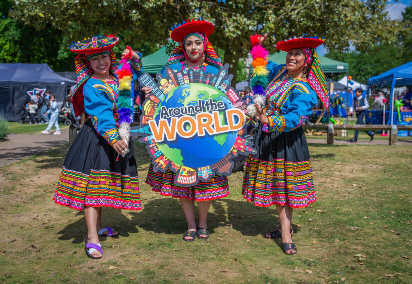 Three women in vibrant, traditional attire stand outdoors, holding a colourful 