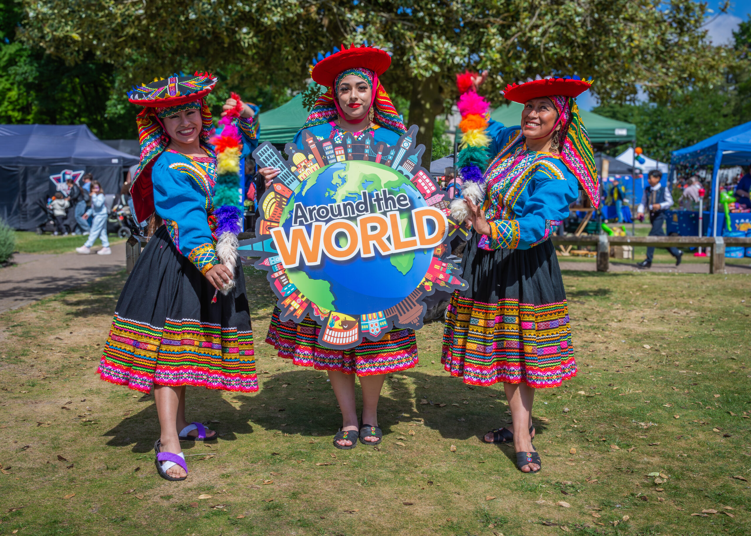 Three women in vibrant, traditional attire stand outdoors, holding a colourful 