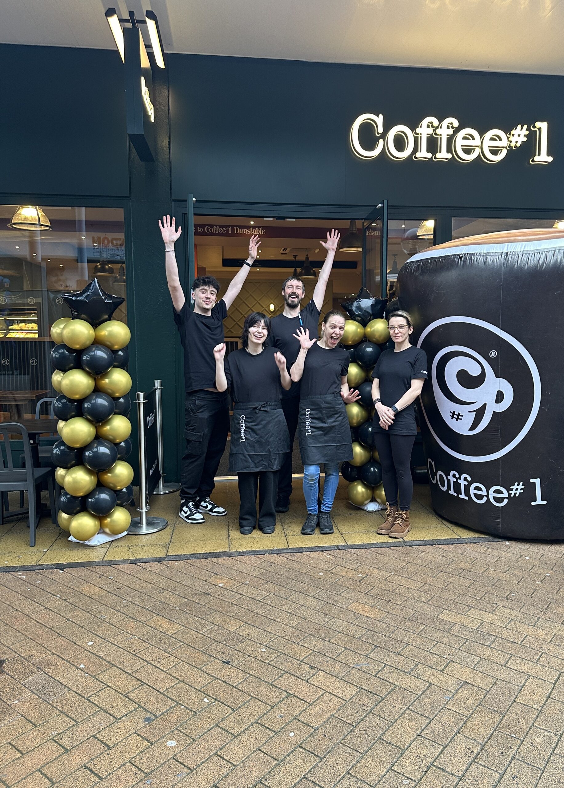 Coffee#1 shop front with staff standing outside with arms in the air