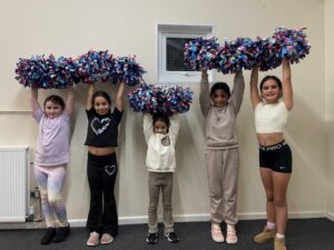 group of young children in a line with pom poms in their hands