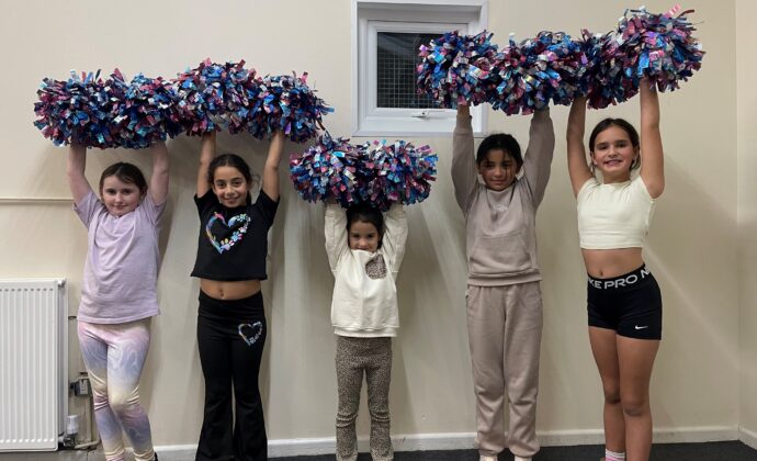 group of young children in a line with pom poms in their hands