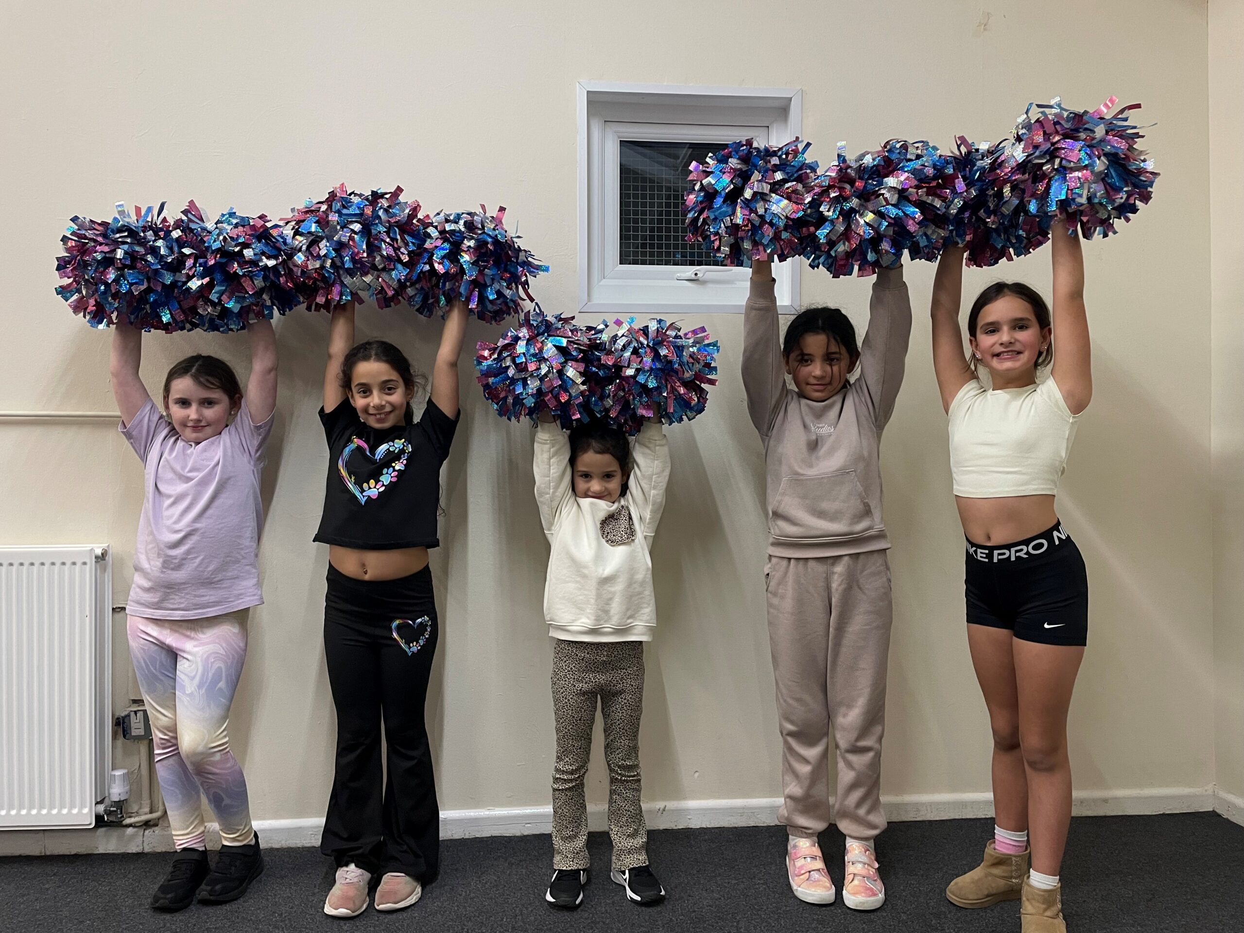 group of young children in a line with pom poms in their hands