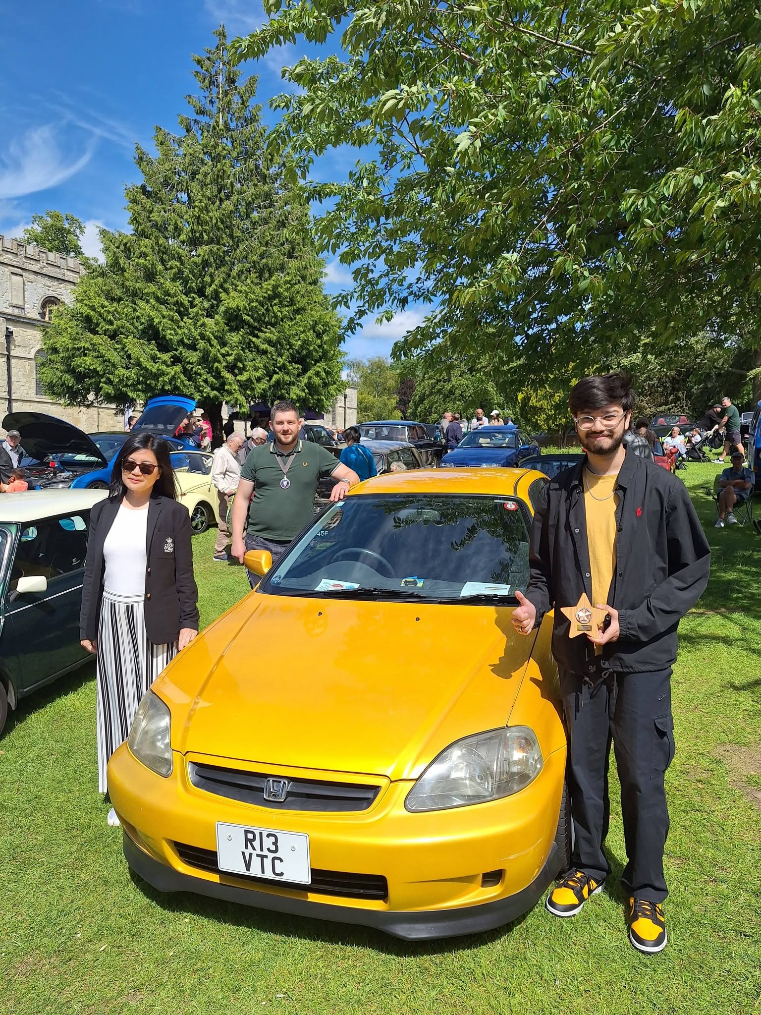 A man and woman pose together next to a yellow car, showcasing a friendly and relaxed atmosphere.