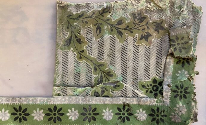 Frayed vintage textile fragment with layered green floral patterns, black-and-white stripes, and decorative borders, evoking a worn, nostalgic mood.