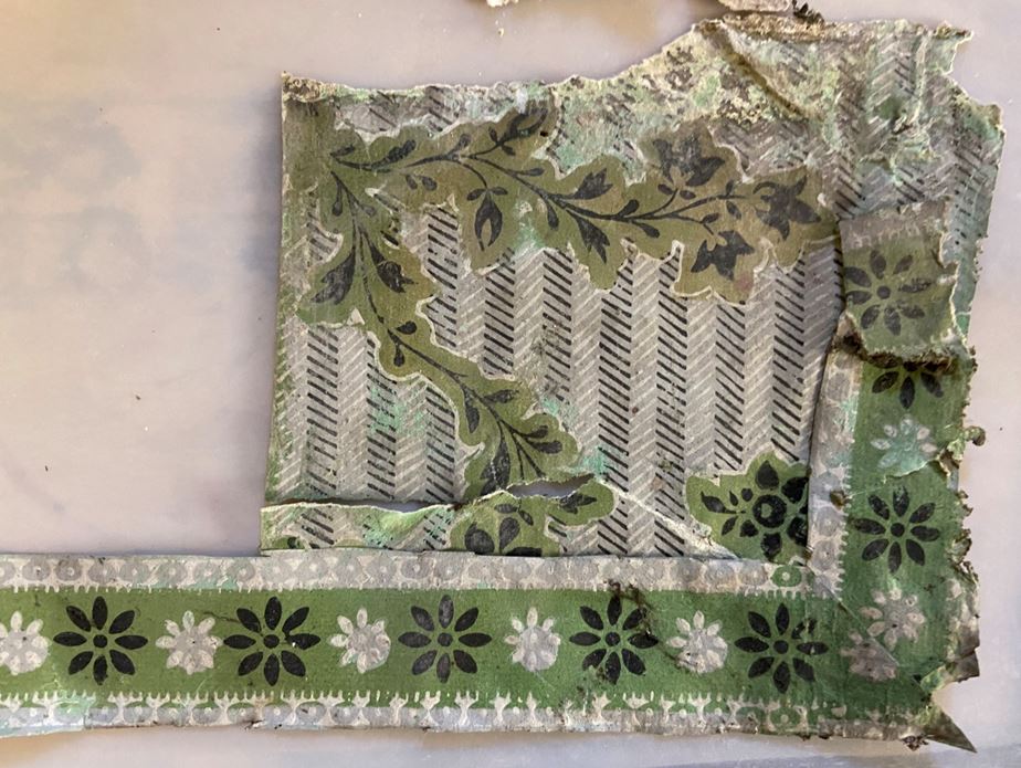 Frayed vintage textile fragment with layered green floral patterns, black-and-white stripes, and decorative borders, evoking a worn, nostalgic mood.